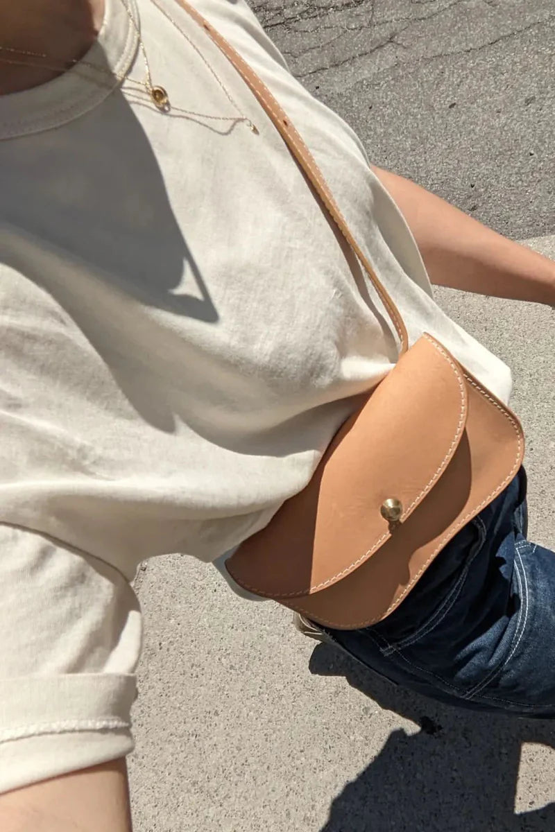 Person wearing a beige shirt with a brown leather crossbody bag on a concrete surface