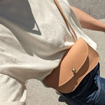 Person wearing a beige shirt with a brown leather crossbody bag on a concrete surface