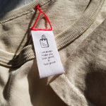 Close-up of a beige garment with a white tag featuring text and a logo.