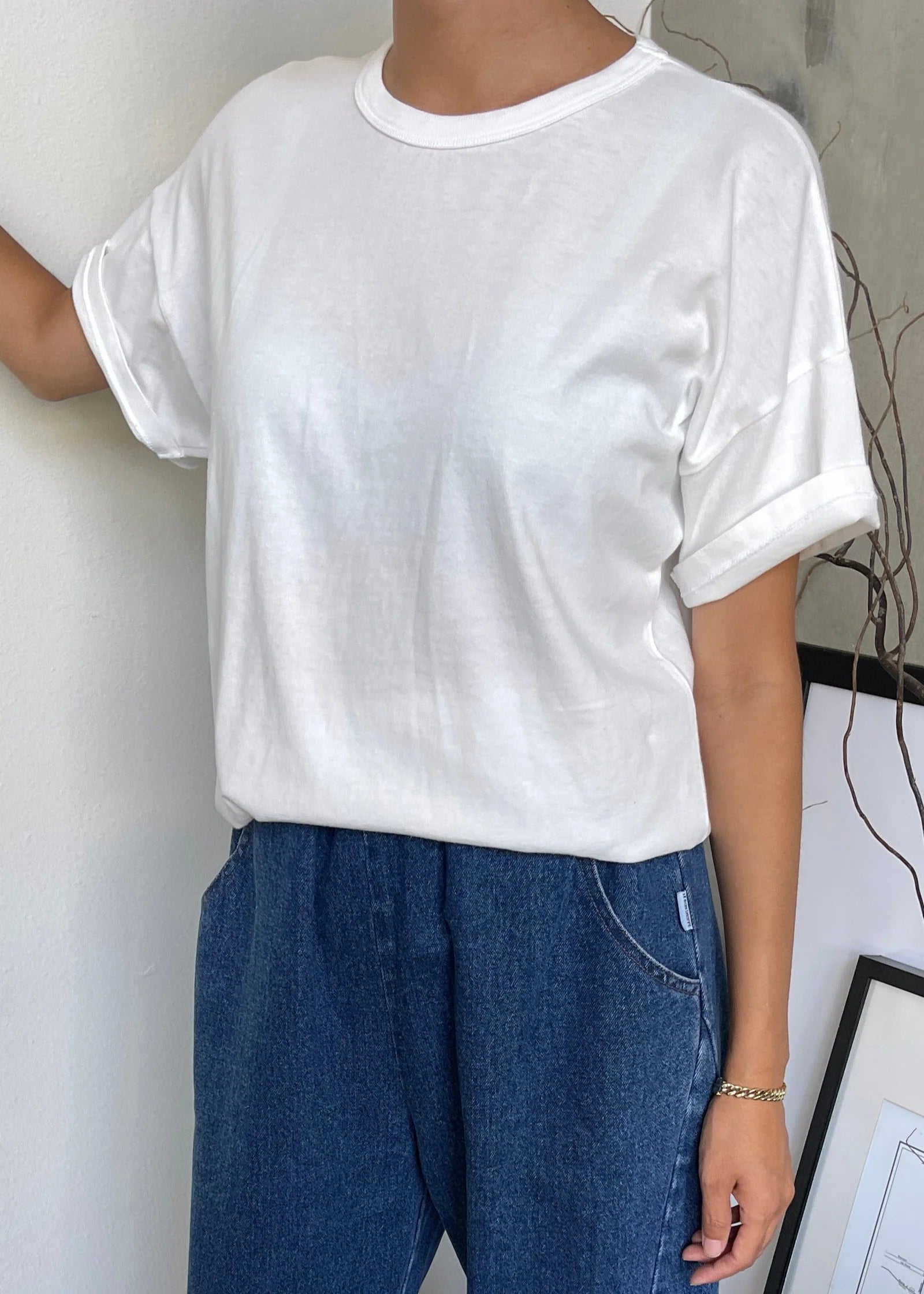 A person wearing a classic white dolman tee-shirt with relaxed fit, paired with blue jeans.