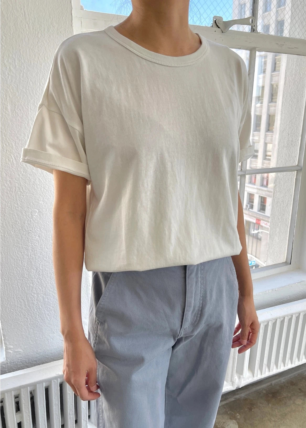 A person wearing a classic white dolman tee-shirt with relaxed fit, paired with blue jeans.