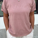 Person wearing a pink t-shirt and white pants standing on a sidewalk.