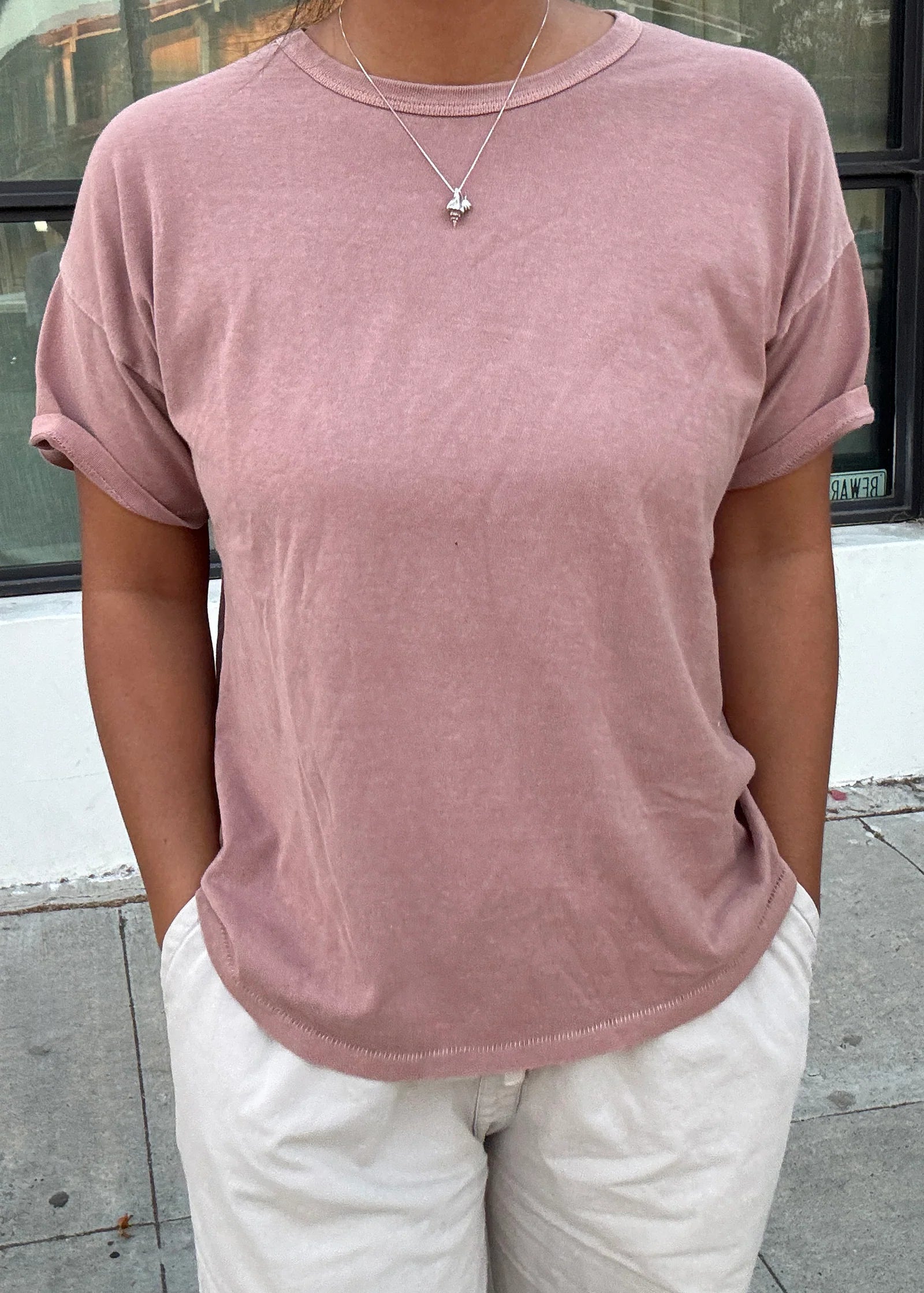 Person wearing a pink t-shirt and white pants standing on a sidewalk.
