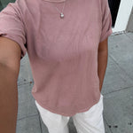 Person wearing a pink t-shirt and white pants on a sidewalk.