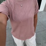 Person wearing a pink t-shirt and white pants on a sidewalk.