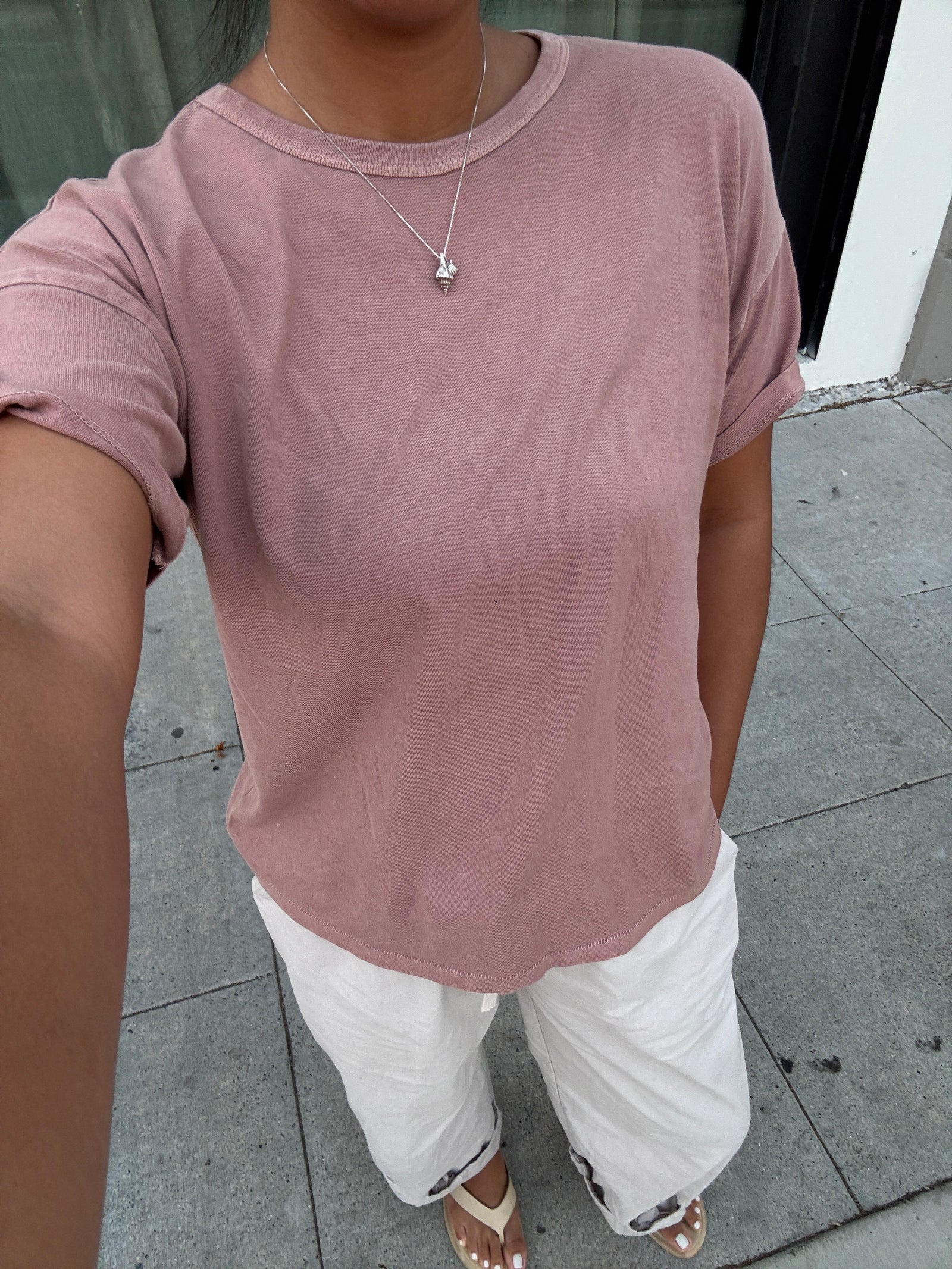 Person wearing a pink t-shirt and white pants on a sidewalk.
