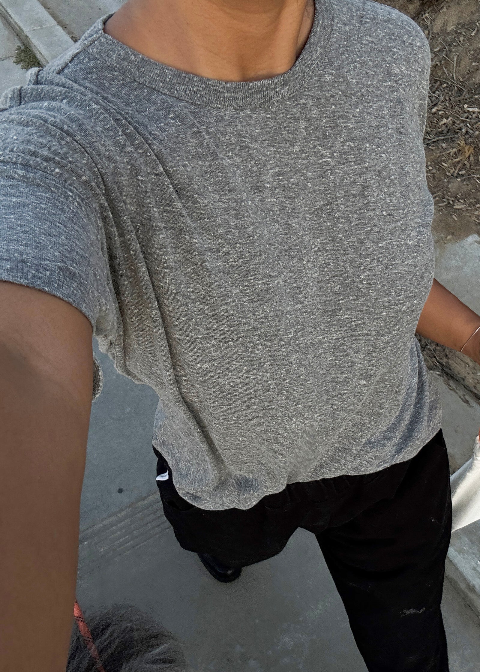Person wearing a gray t-shirt and black pants on a concrete surface.