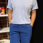 Person wearing a light gray t-shirt and blue pants standing in front of a dark background.