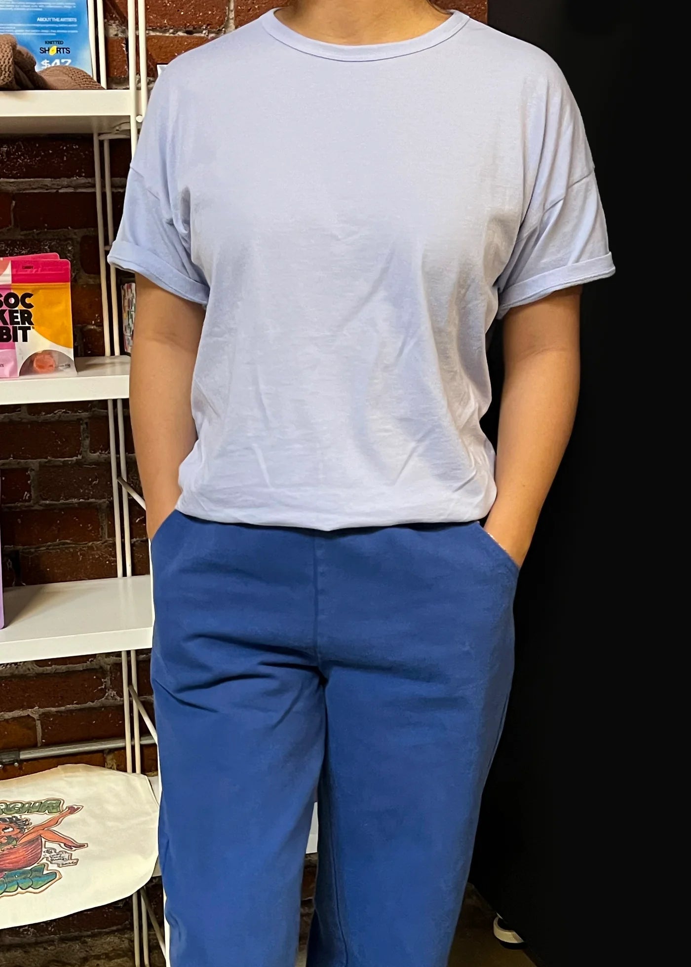 Person wearing a light gray t-shirt and blue pants standing in front of a dark background.