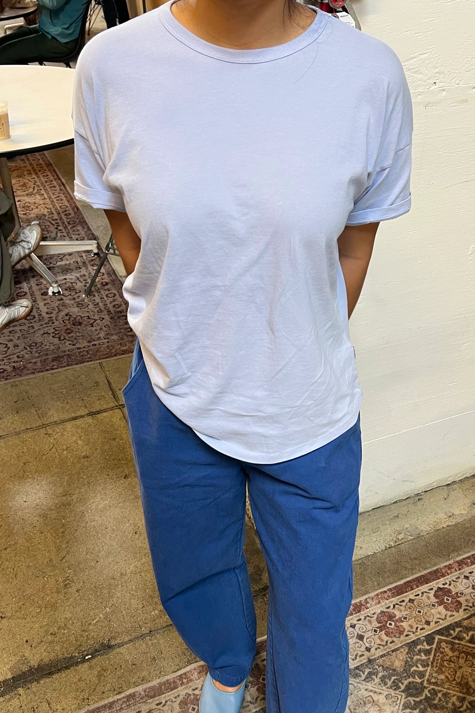 Person wearing a light blue t-shirt and blue pants in an indoor setting.