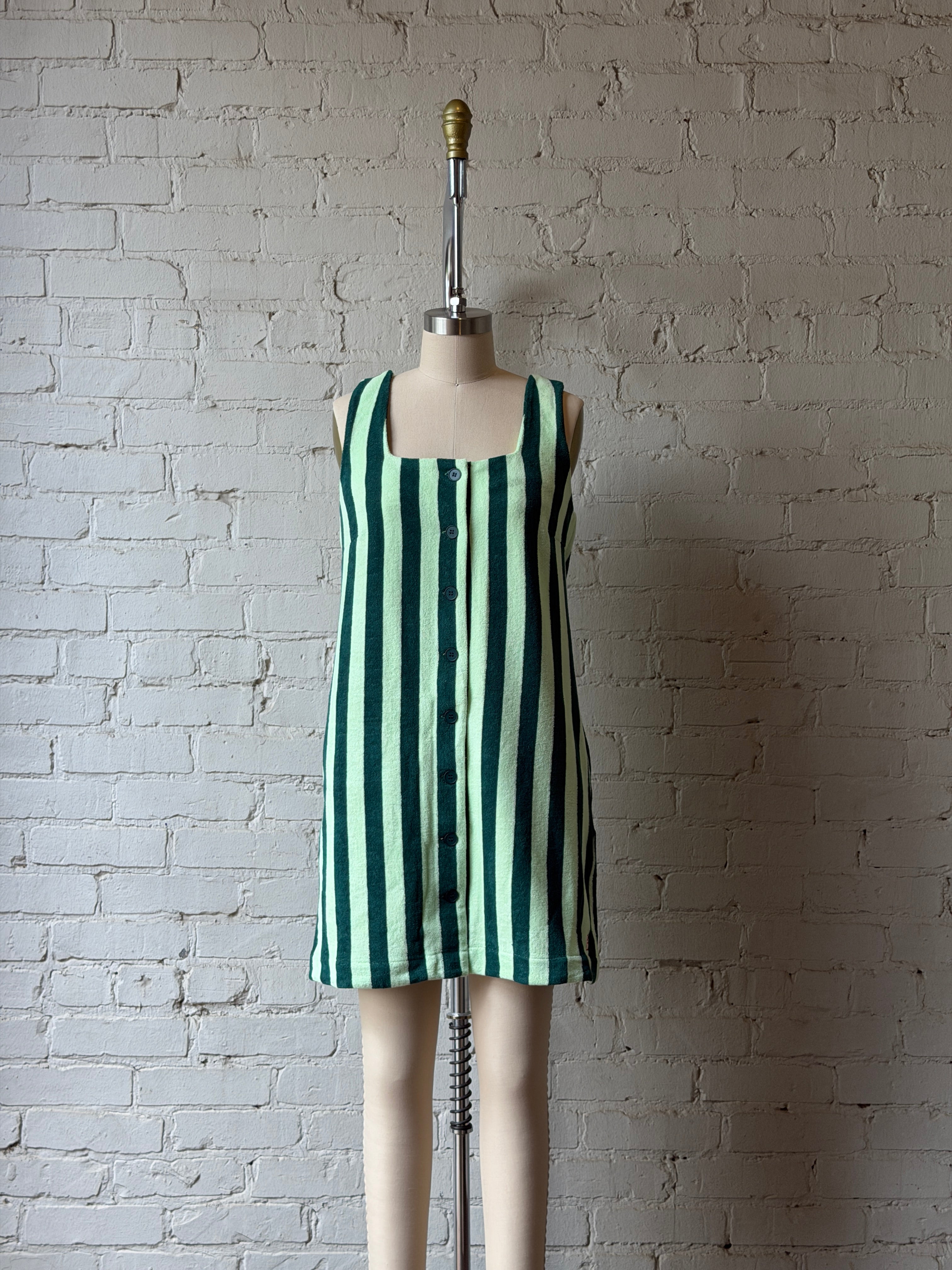Green and white striped dress on a mannequin against a textured wall.