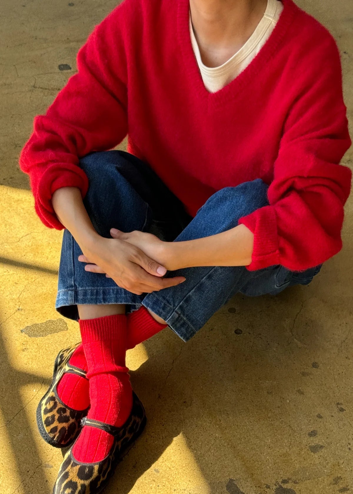 Person wearing a red sweater, blue jeans, red socks, and leopard print shoes on a yellow floor.