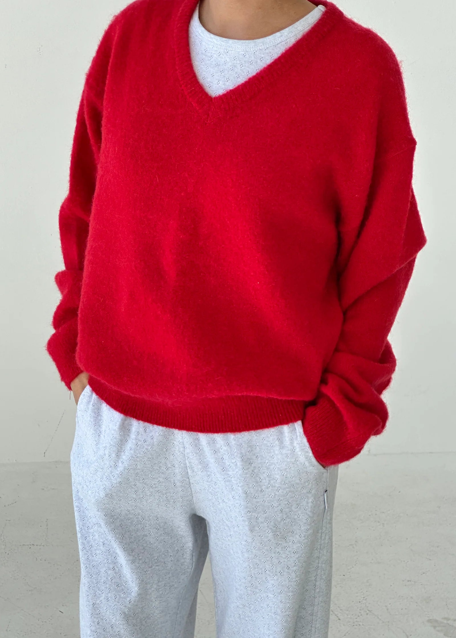 Person wearing a red sweater over a white shirt with gray pants against a plain background