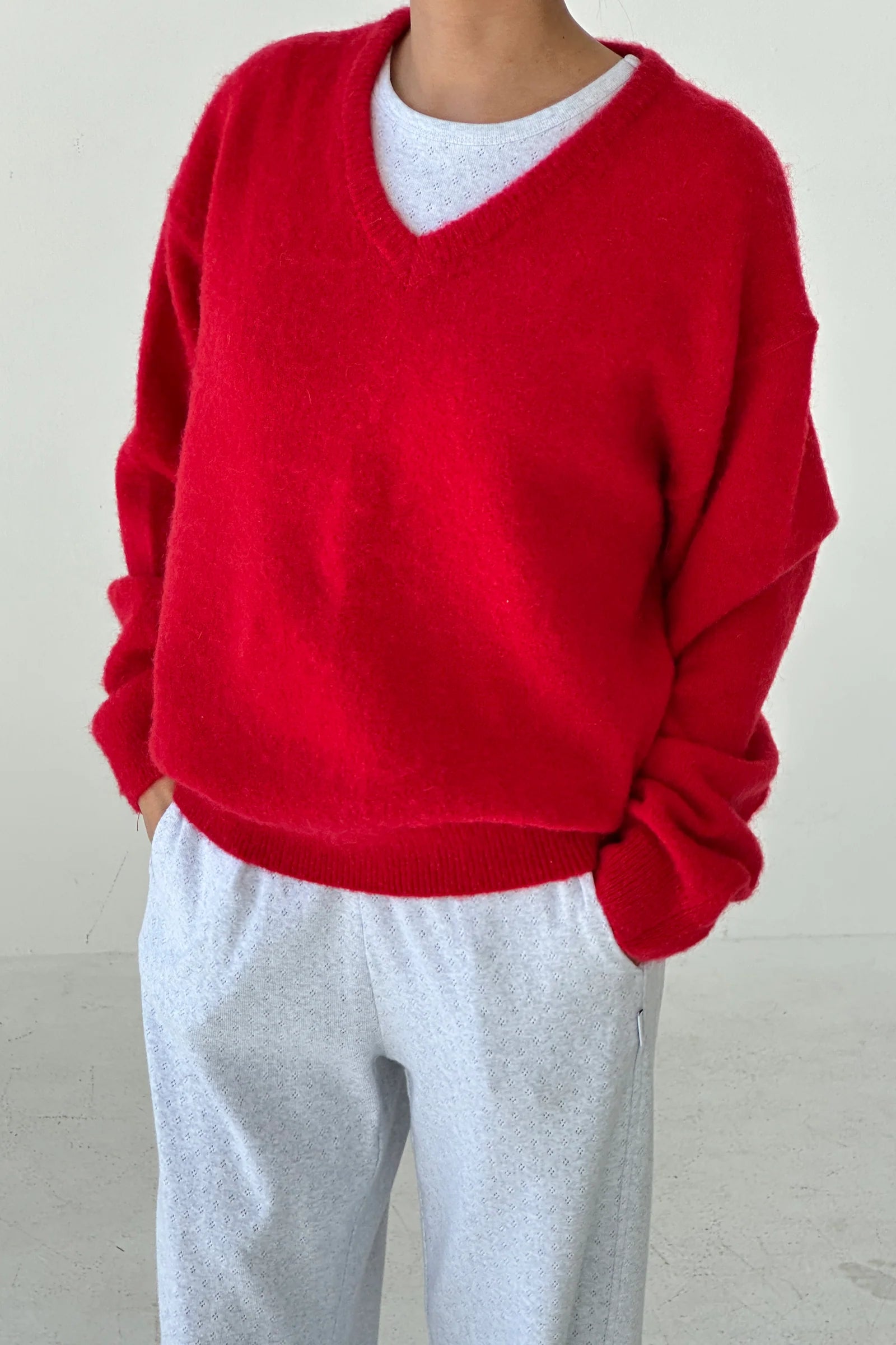 Person wearing a red sweater over a white shirt with gray pants against a plain background