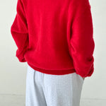 Person wearing a red sweater and light gray pants on a white background
