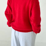 Person wearing a red sweater and light gray pants on a white background