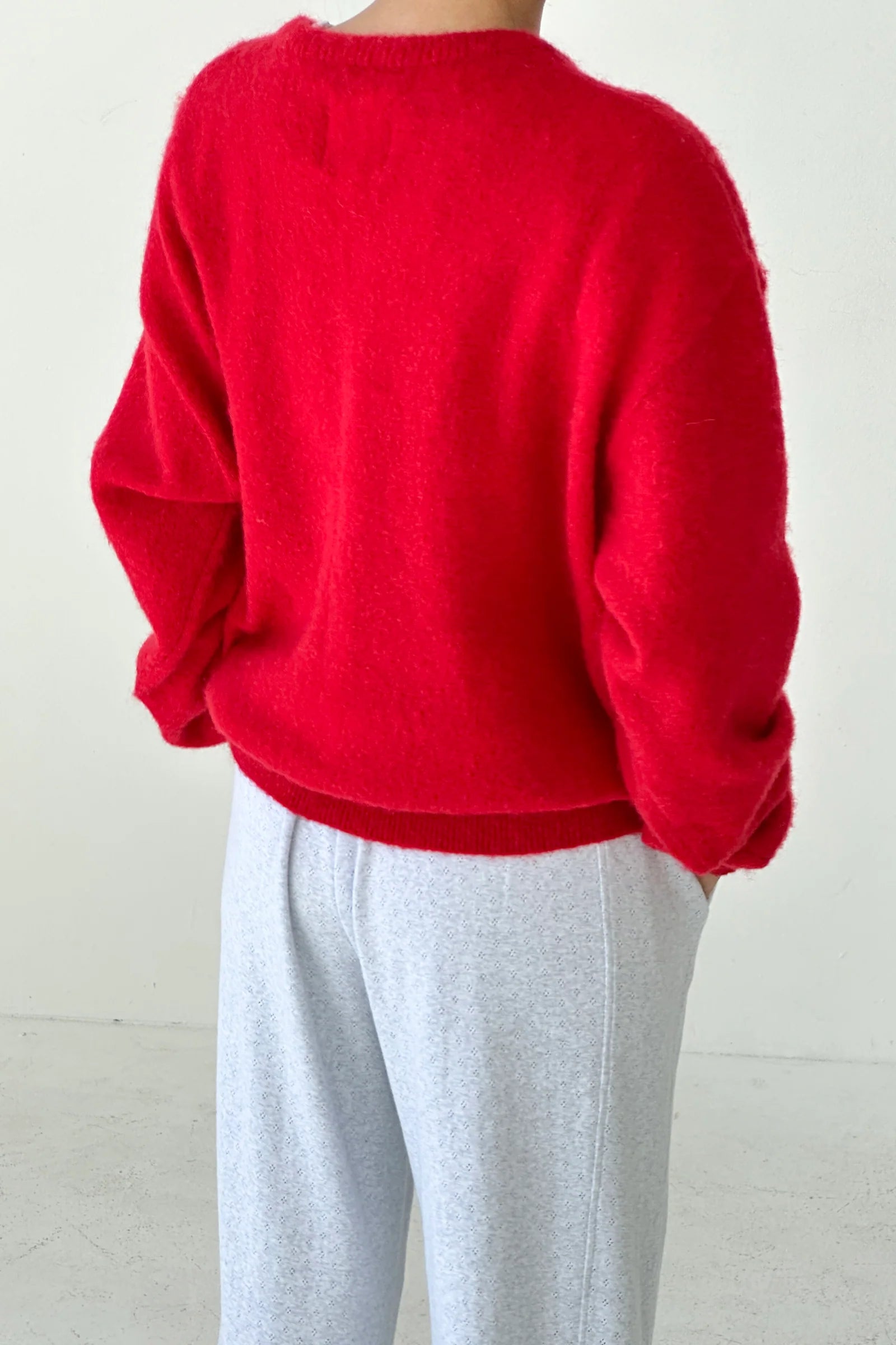 Person wearing a red sweater and light gray pants on a white background