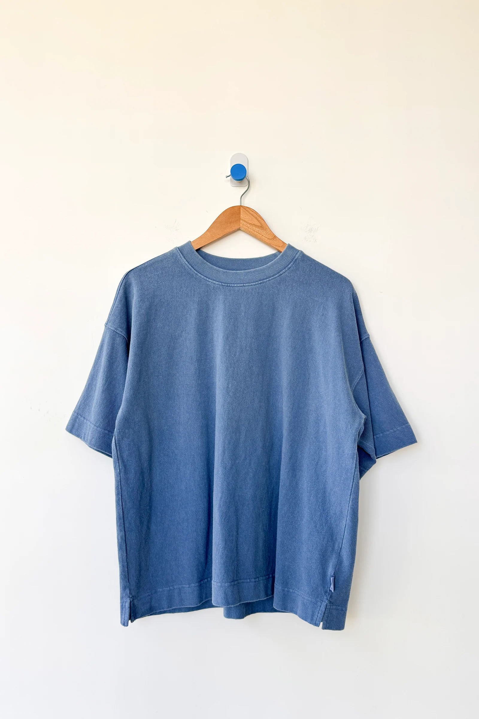 Blue t-shirt on a wooden hanger against a white background