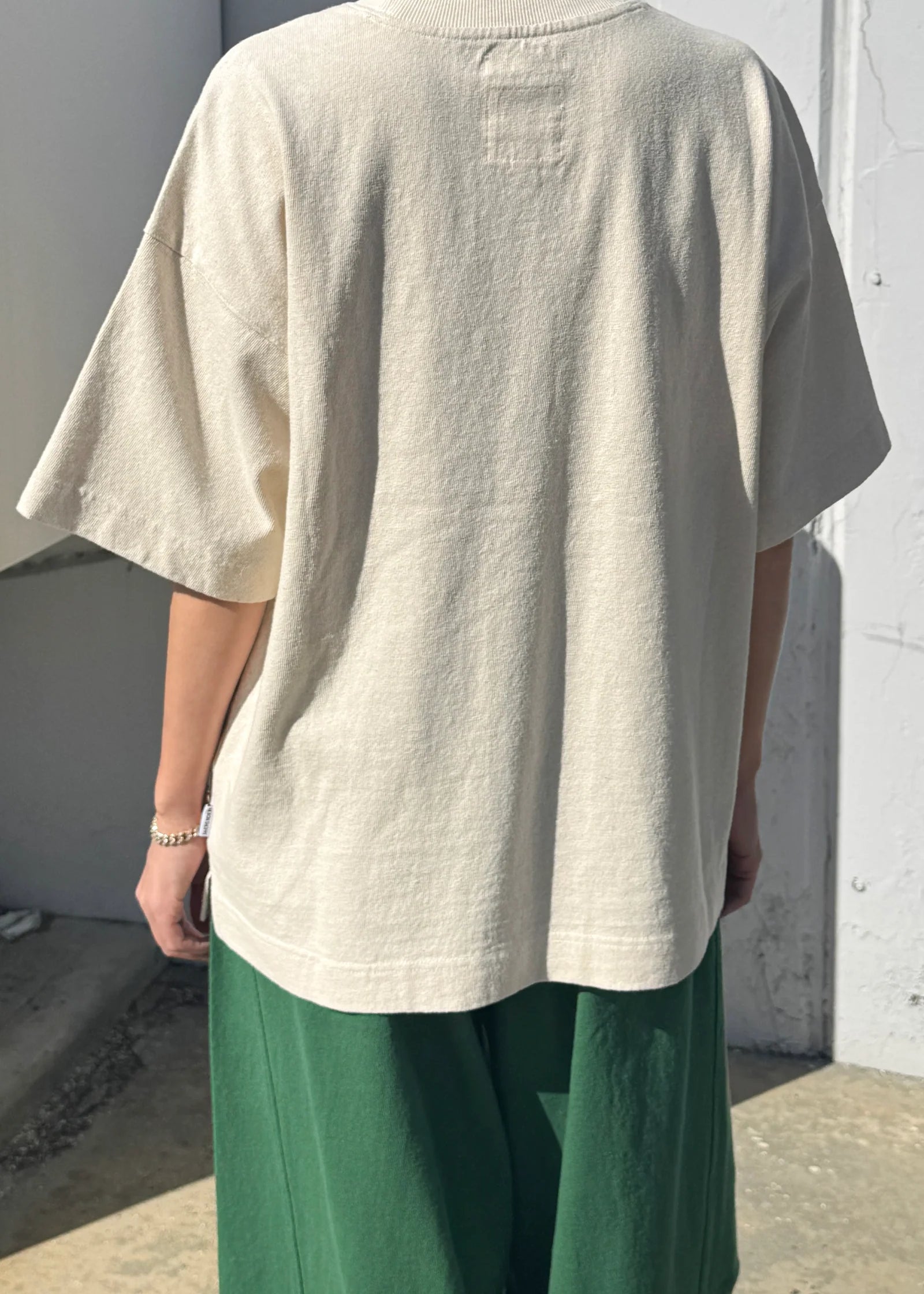 Person wearing a beige oversized t-shirt and green pants against a plain wall.
