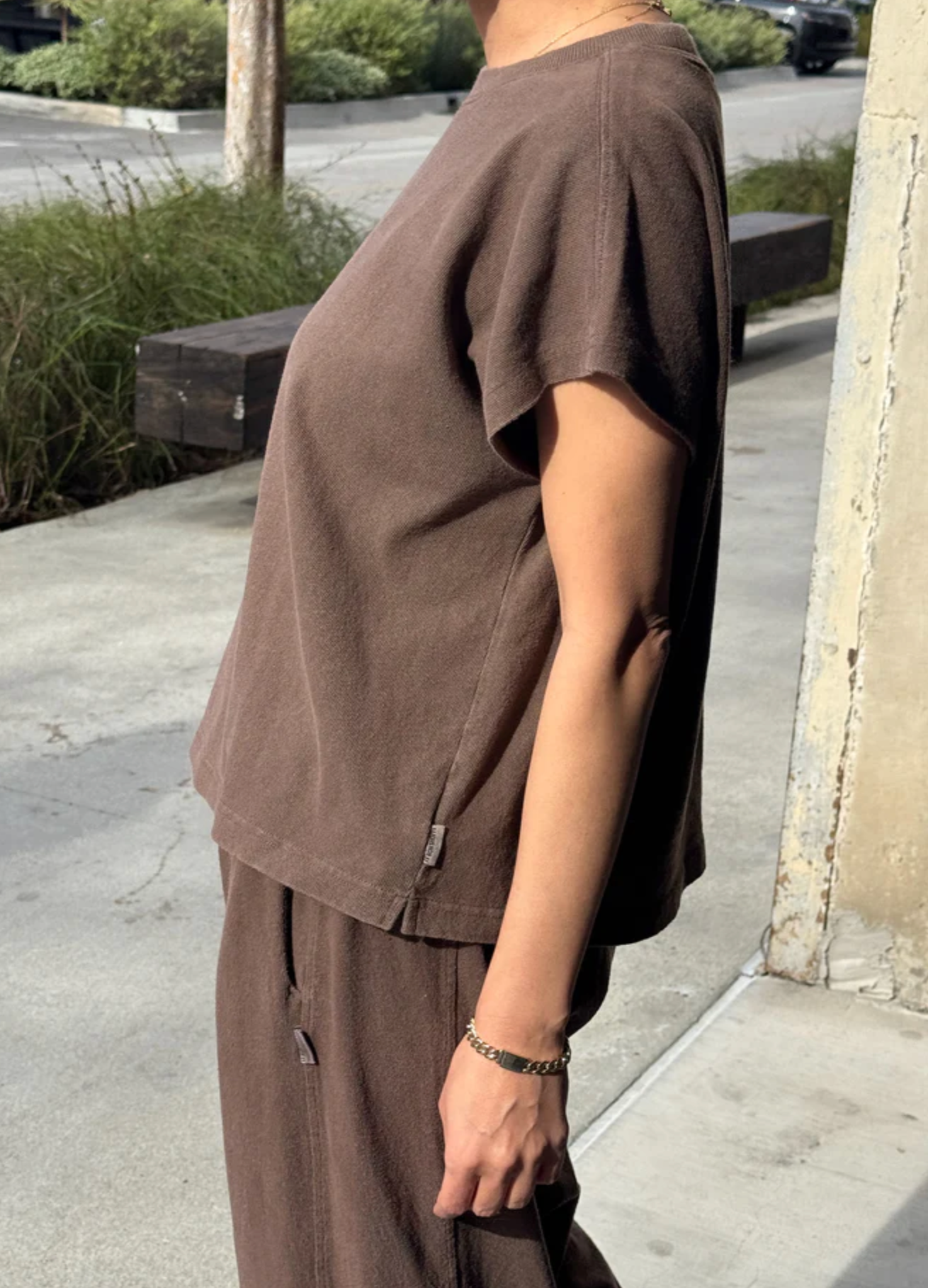 Person wearing a brown outfit standing on a sidewalk.