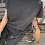 Person wearing a black outfit sitting on a wooden bench outdoors.