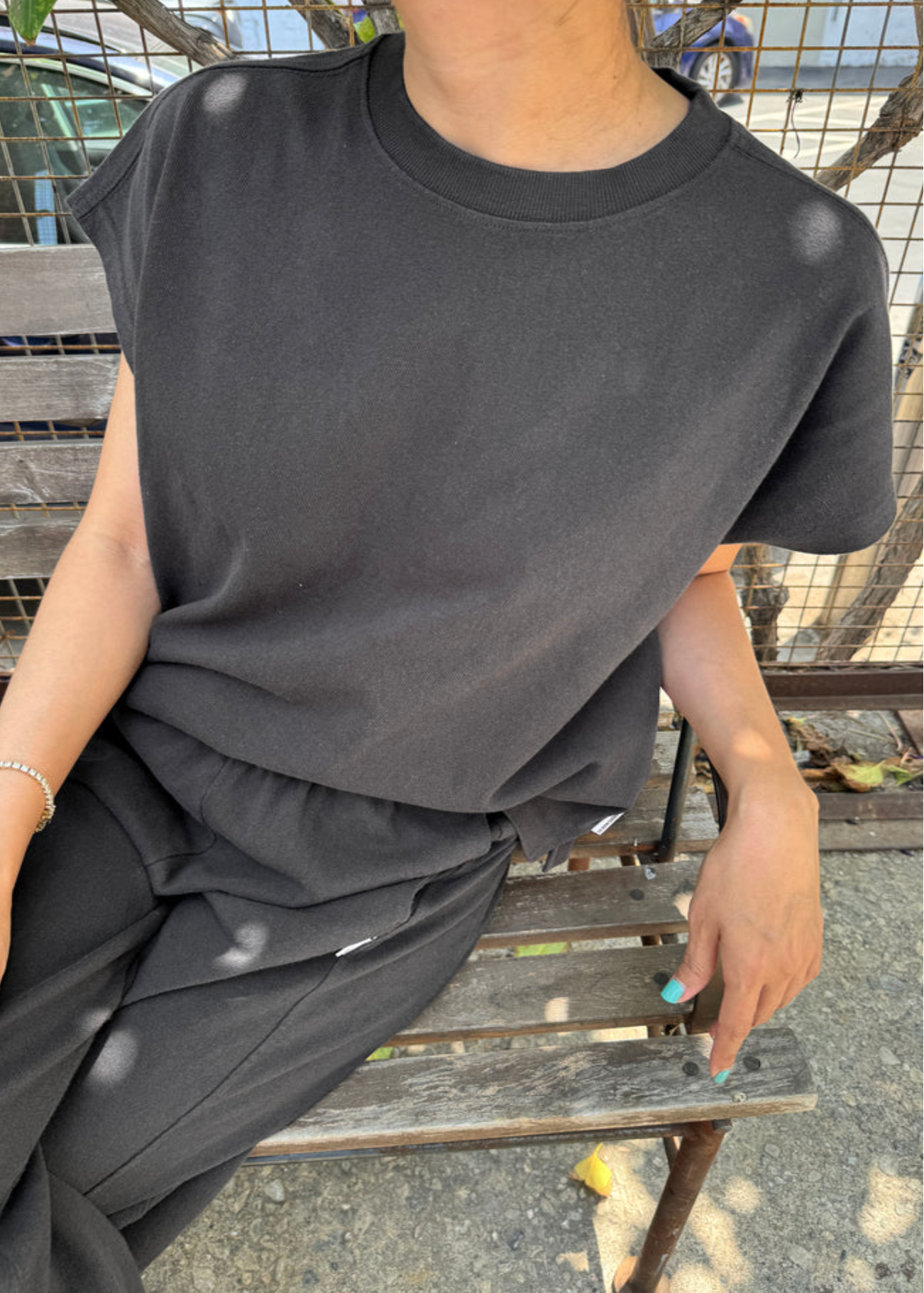 Person wearing a black outfit sitting on a wooden bench outdoors.