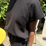 Person wearing a dark gray t-shirt and pants outdoors with greenery in the background