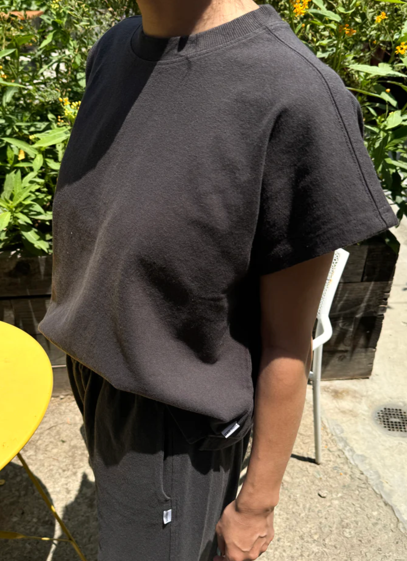 Person wearing a dark gray t-shirt and pants outdoors with greenery in the background