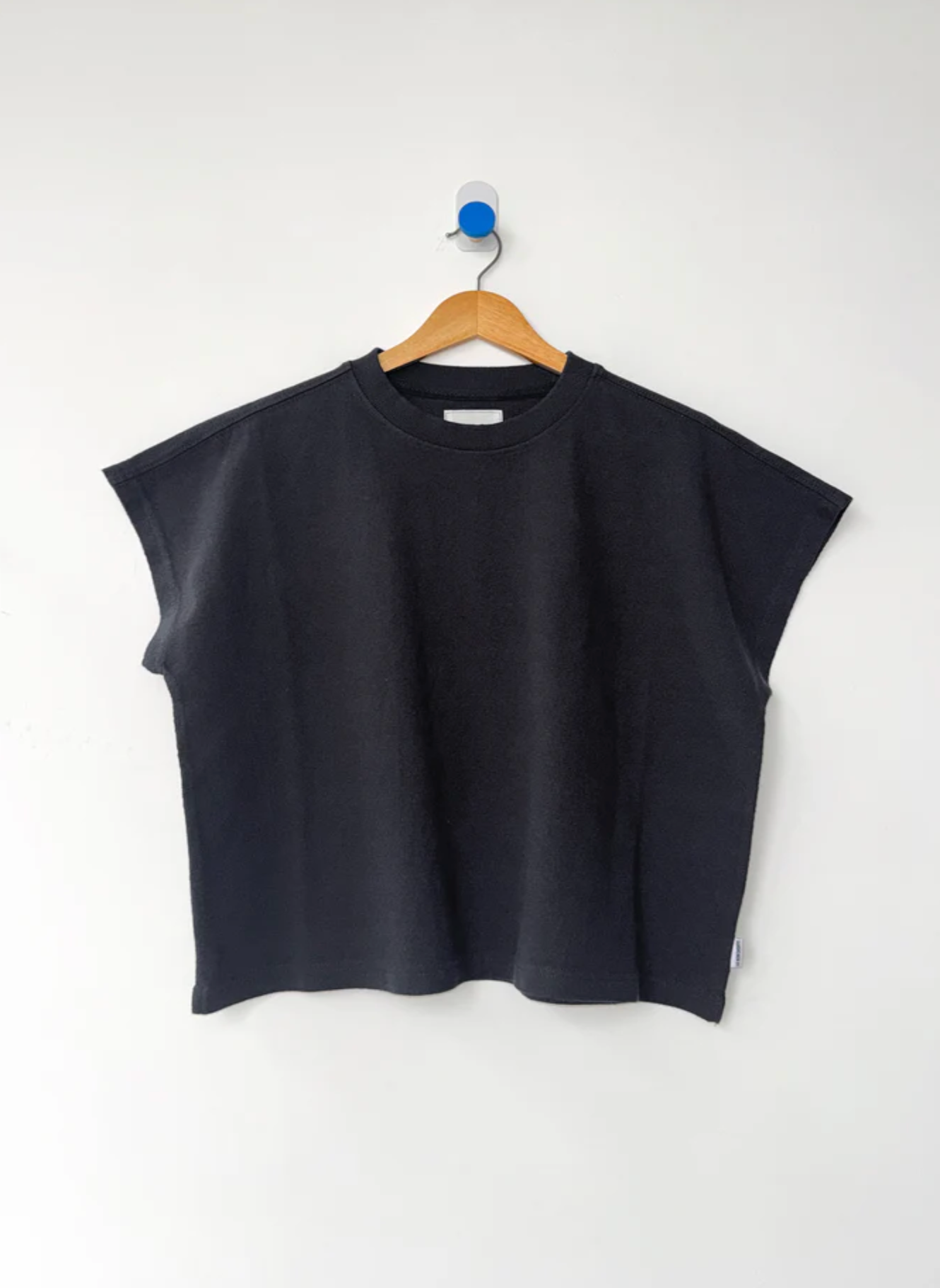 Black sleeveless top on a wooden hanger against a white background
