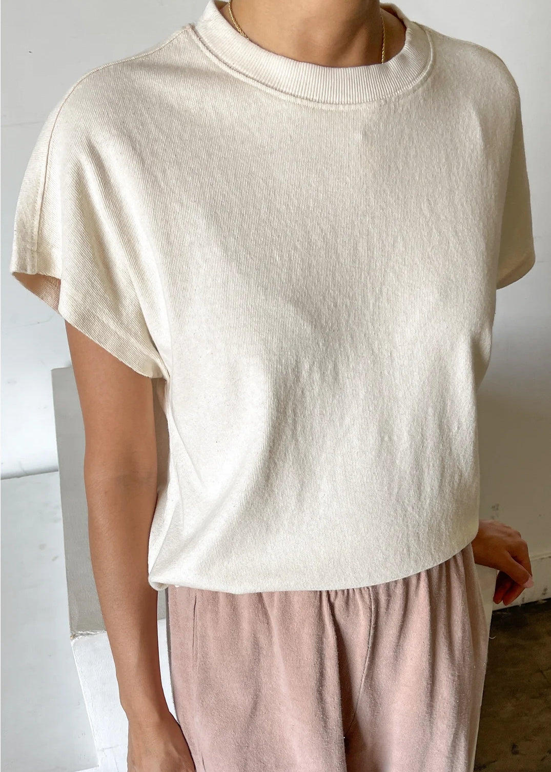 Person wearing a beige sweater and pink pants against a neutral background