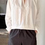Person wearing a white blouse and dark pants in an indoor setting