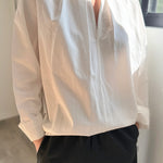 Person wearing a light-colored blouse with long sleeves and dark pants indoors.