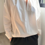 Person wearing a light-colored blouse with long sleeves and dark pants indoors.