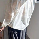 White blouse with long sleeves and a high collar worn by a person, standing against a neutral background.