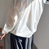 White blouse with long sleeves and a high collar worn by a person, standing against a neutral background.