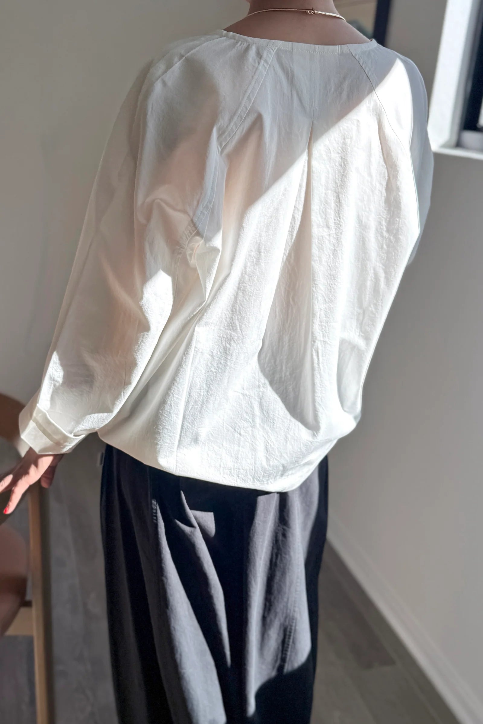 White blouse with long sleeves and a high collar worn by a person, standing against a neutral background.