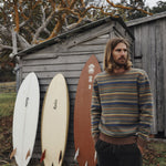 Man standing next to surfboards against a wooden shed