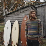 Man standing next to surfboards against a wooden shed