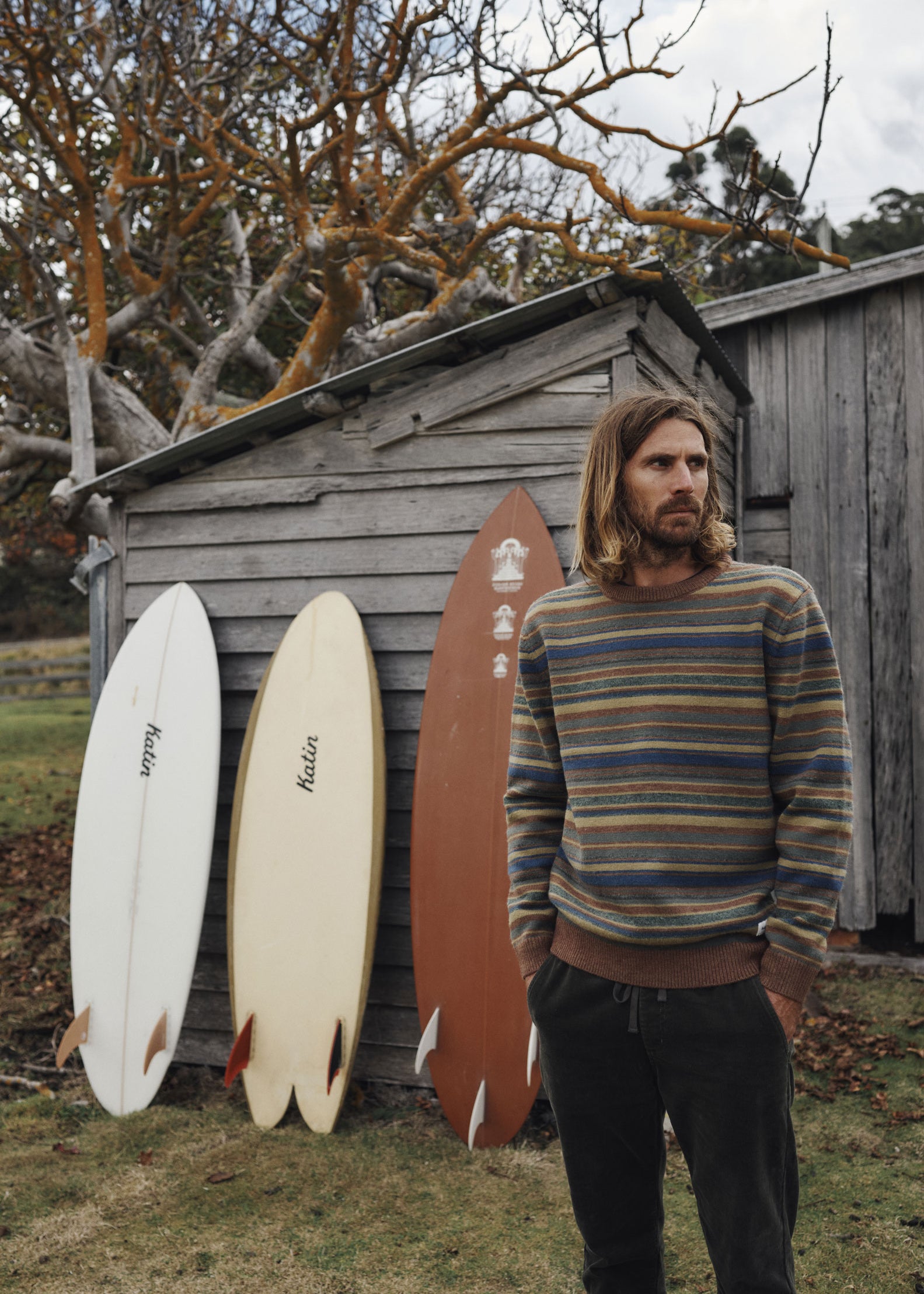 Man standing next to surfboards against a wooden shed