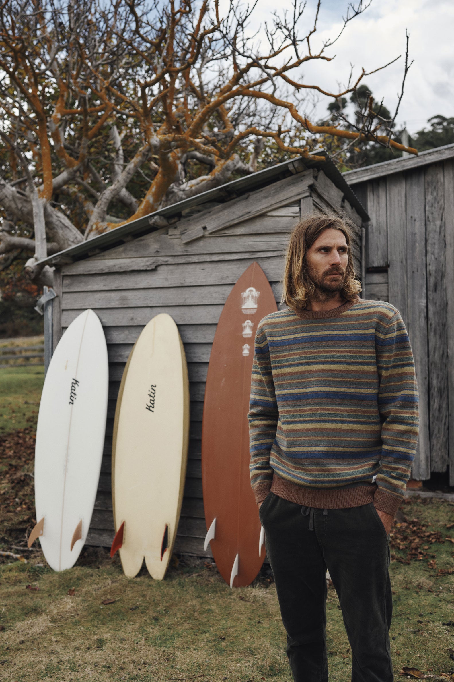 Man standing next to surfboards against a wooden shed