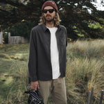 Man standing outdoors in a natural setting wearing sunglasses, a beanie, and casual clothing.