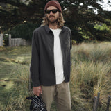 Man standing outdoors in a natural setting wearing sunglasses, a beanie, and casual clothing.