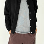 Person wearing a black cardigan over a gray shirt with brown pants on a white background