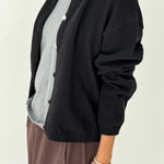Person wearing a black cardigan over a gray shirt with a beige background