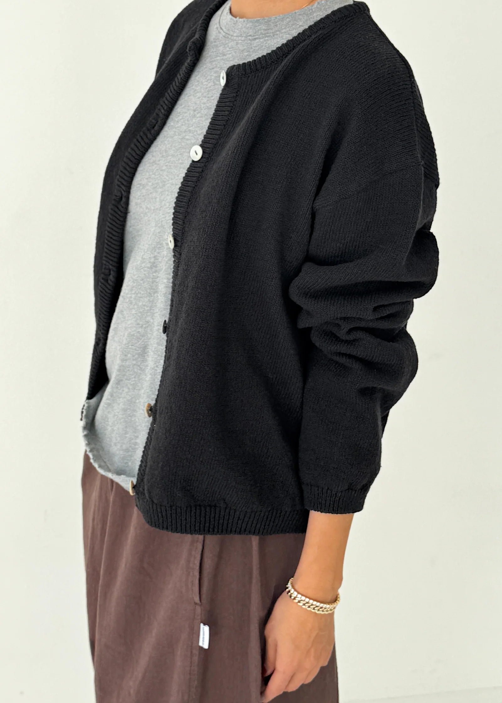 Person wearing a black cardigan over a gray shirt with a beige background