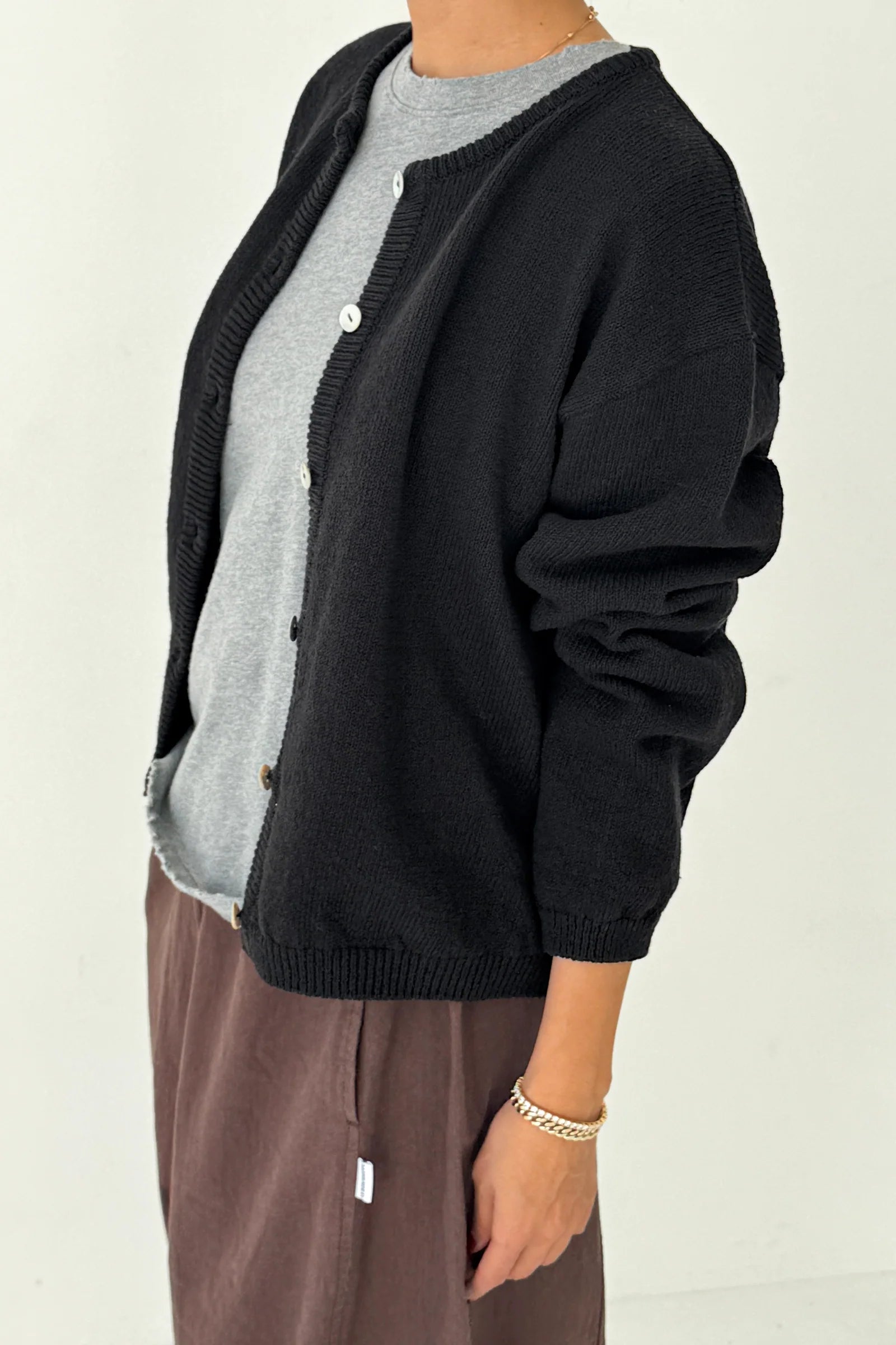 Person wearing a black cardigan over a gray shirt with a beige background