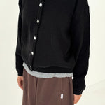Person wearing a black cardigan with white buttons on a plain background