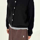 Person wearing a black cardigan with white buttons on a plain background