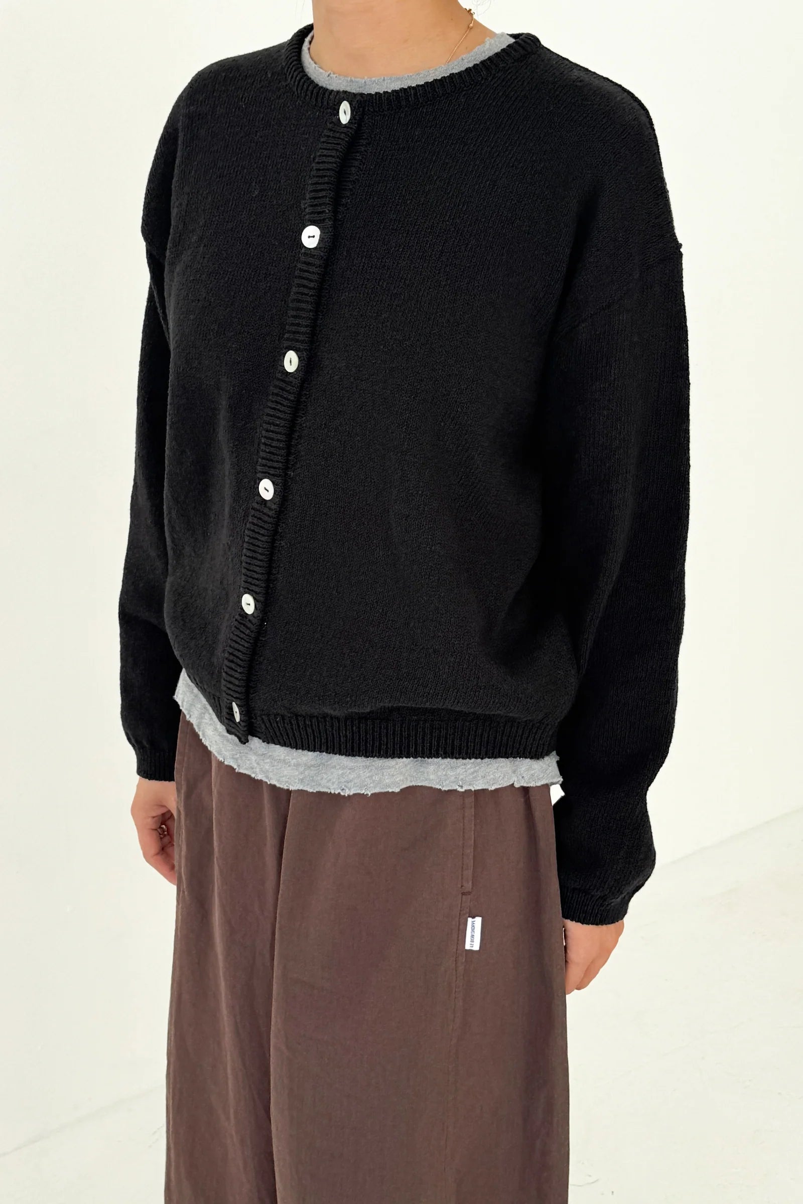 Person wearing a black cardigan with white buttons on a plain background