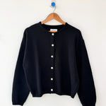 Black cardigan on a wooden hanger against a white background